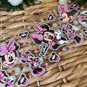 May include: Clear stickers featuring Minnie Mouse in various poses, with pink bows and polka dots. The stickers also include cupcake and flower designs, with the word "Minnie" in cursive.