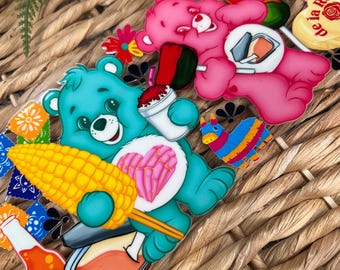 May include: A collection of colorful, cartoon-style stickers featuring Care Bears with food and drink items. The stickers include a blue bear with corn, a pink bear with sushi, and various beverage and food-themed designs.