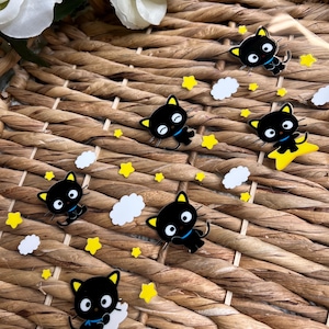 May include: A sheet of black and white stickers featuring a cartoon black cat with a blue bow tie. The cat is on a white cloud with yellow stars in the background.