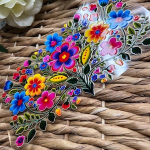 May include: A colorful floral design with bright pink, yellow, blue, and green flowers on a clear background. The design is reminiscent of traditional Mexican folk art.