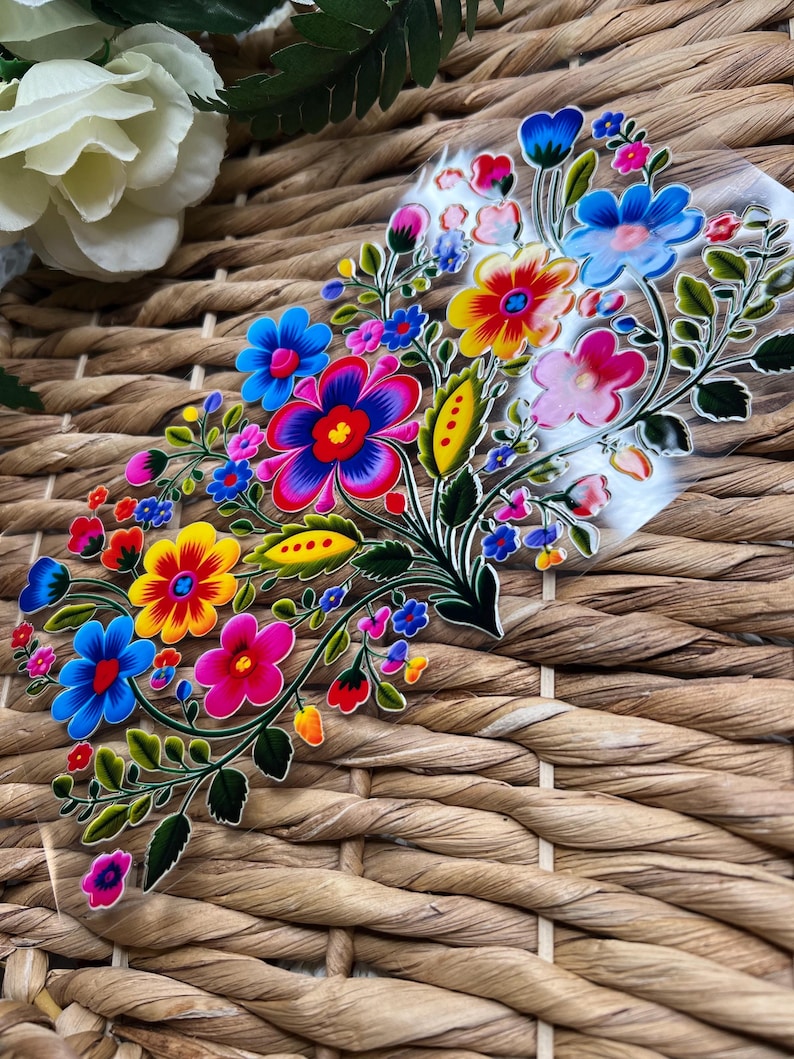 May include: A colorful floral design with bright pink, yellow, blue, and green flowers on a clear background. The design is reminiscent of traditional Mexican folk art.