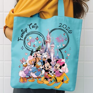 May include: A turquoise tote bag with a Disney-themed design. It features Mickey and Minnie Mouse, Donald Duck, and Goofy, with the words "Family Trip 2026" and a castle illustration. The bag has a simple, practical design.