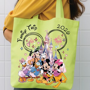 May include: A light green tote bag with a colourful illustration of Disney characters and a castle. The words "Family Trip 2026" are written on the bag. The bag has green handles.