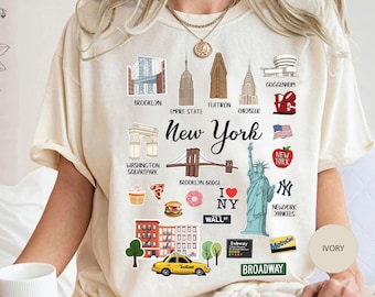 Puede incluir: Una camiseta color marfil con un estampado gráfico de monumentos e iconos de la ciudad de Nueva York, incluyendo la Estatua de la Libertad, el puente de Brooklyn, el Empire State Building y un taxi amarillo. El texto incluye New York, Brooklyn, Wall St y Broadway.