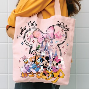 May include: A pink tote bag with a Disney design. The bag features Mickey Mouse, Minnie Mouse, Donald Duck, Daisy Duck, Goofy, and Pluto in front of a castle. The words "Family Trip 2026" are printed on the bag.