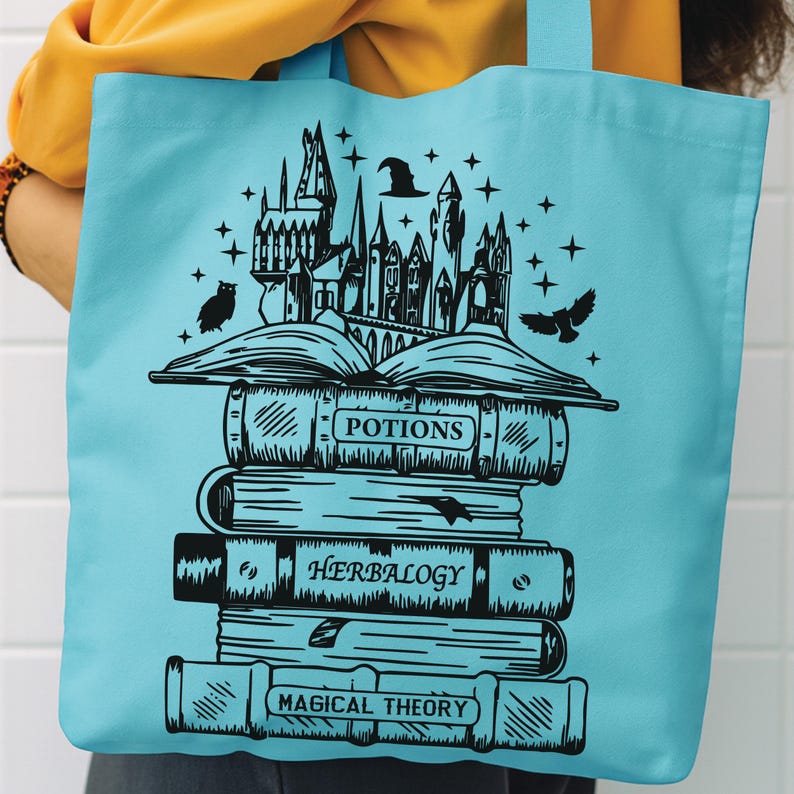 May include: A light blue tote bag featuring a black graphic print of a stack of books titled Potions, Herbalogy, and Magical Theory. An open book sits atop the stack, topped with a castle silhouette, a witch hat, stars, and two owls.