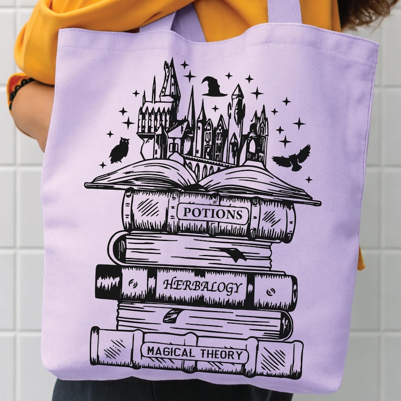 May include: A light purple tote bag featuring a black graphic print of a stack of books topped with a castle, an owl, and a witch hat. The book spines are labelled with the text Potions, Herbalogy, and Magical Theory in a clear, bold font.