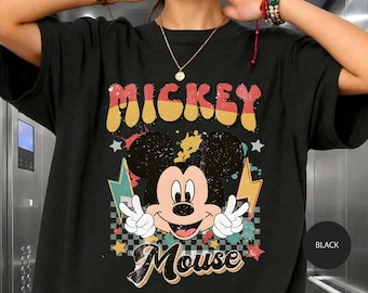 Peut inclure: Un t-shirt noir avec un motif de Mickey Mouse faisant un signe de paix. Le design comprend le texte "MICKEY" en jaune et "Mouse" en blanc, entouré d'éclairs colorés, d'étoiles et d'un motif à damier noir et blanc sur le devant.