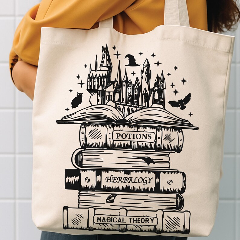 May include: A cream-coloured canvas tote bag featuring a black graphic print of a stack of books. The design includes an open book topped with a castle, owls, and stars. The book spines are labelled Potions, Herbalogy, and Magical Theory.
