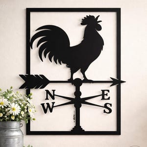 Puede incluir: Veleta de metal negro con diseño de gallo y flechas direccionales, montada sobre fondo blanco. Con letras N, E, S y W. En primer plano, un jarrón de metal galvanizado con flores blancas.