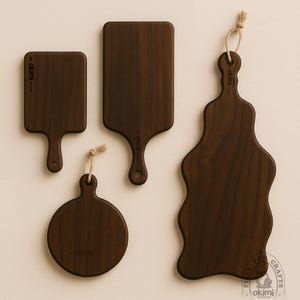 Puede incluir: Cuatro tablas de cortar de madera marr&oacute;n oscuro de varias formas. Dos tablas rectangulares con asas, una tabla redonda y una tabla de forma &uacute;nica. Cada tabla tiene una veta de madera natural y un peque&ntilde;o lazo para colgar. Las tablas est&aacute;n etiquetadas con "by okimi".