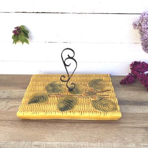 Peut inclure: Un porte-serviettes en céramique jaune avec un motif tissé et un motif de feuille en métal noir. Le porte-serviettes est sur une surface en bois.
