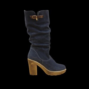 The detail on the boot features a piece of leather resembling a strap with a metal clip. A decorative leather strap with a buckle on the upper part and side of the boot.