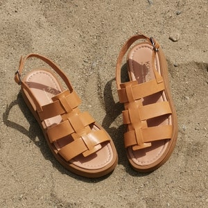May include: A pair of tan leather sandals with a woven design. The sandals have a buckle closure and a thick sole.