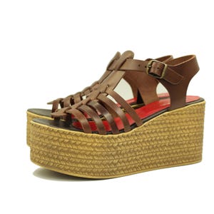 May include: Brown leather platform sandals with woven jute soles. The sandals have a cage-like design with multiple straps and a buckle closure. The platform sole measures approximately 7.6 cm in height.