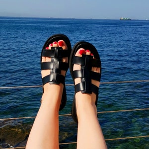 May include: A pair of black leather sandals with a woven design. The sandals have red nail polish on the toes.