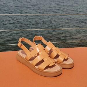 May include: A pair of tan leather sandals with a woven design and a thick platform sole. The sandals have a buckle closure at the ankle.
