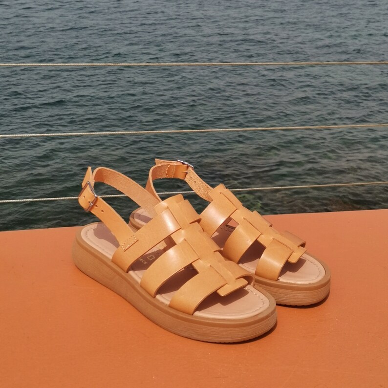 May include: A pair of tan leather sandals with a woven design and a thick platform sole. The sandals have a buckle closure at the ankle.