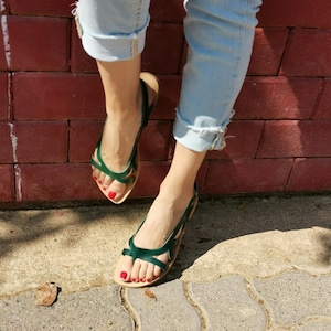 May include: A pair of green leather sandals with a criss-cross strap design. The sandals have a slingback strap and are worn on a person's feet.
