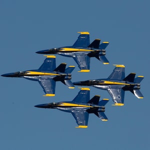 Puede incluir: Cuatro aviones de combate azules y amarillos vuelan en formación contra un cielo azul claro.