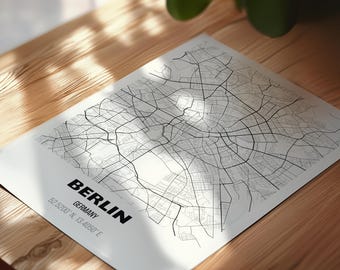 Może przedstawiać: Biały nadruk mapy miasta Berlin, Niemcy. Mapa przedstawia sieć czarnych linii reprezentujących ulice i drogi. Nazwa miasta i współrzędne są wydrukowane na czarno. Nadruk znajduje się na drewnianej powierzchni.