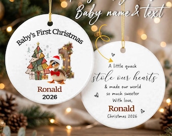 Op de afbeelding: Twee ronde witte keramische ornamenten met gouden ophangkoorden. Eén toont een patchwork kerstboom, een eendje met een kerstmuts en de tekst Baby's First Christmas, Ronald, 2026. De andere toont A little quack stole our hearts, Ronald, en Christmas 2026.