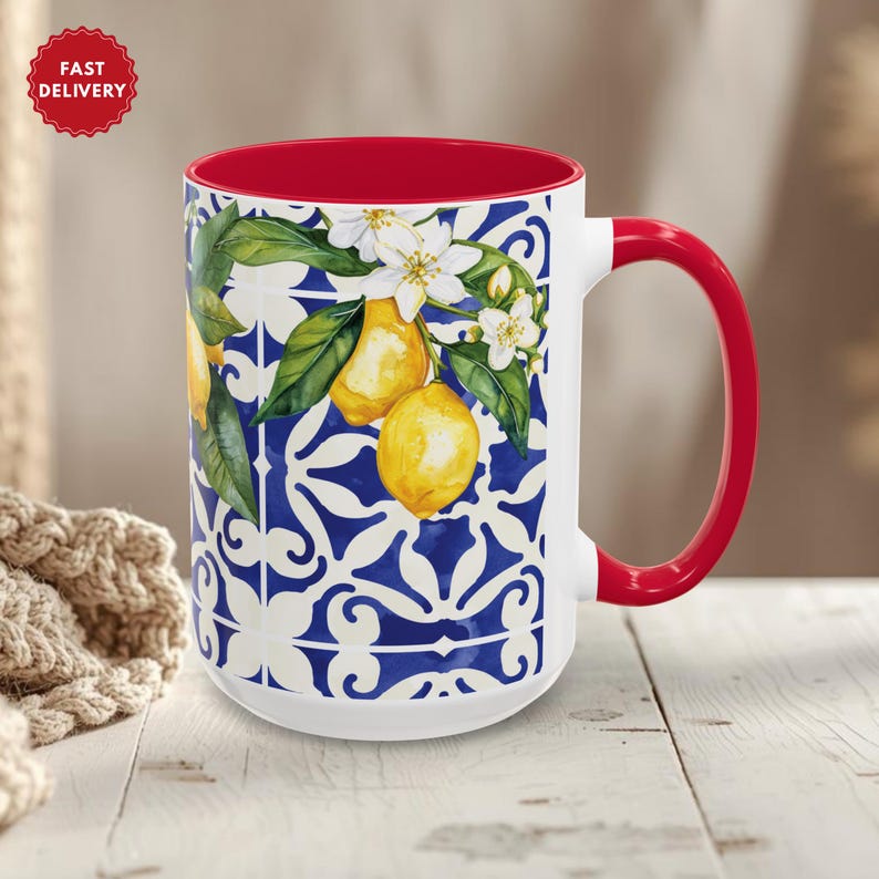 May include: White ceramic mug with a red interior and handle. The mug features a blue and white patterned design with yellow lemons, green leaves, and white flowers. A red "Fast Delivery" sticker is visible.