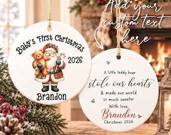 Op de afbeelding: Twee ronde witte keramische ornamenten met gouden ophangkoorden. Eén toont een Kerstman met een teddybeer en de tekst Baby's First Christmas 2026 en Brandon. De andere toont de tekst A little teddy bear stole our hearts.