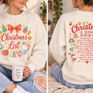 May include: A cream-colored crewneck sweatshirt featuring a front graphic of a red bow and the text Christmas List surrounded by holiday icons. The back displays the text Christmas List with a checklist of festive activities and illustrations.