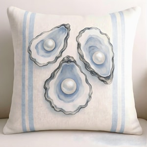 May include: Square decorative pillow with a watercolor design of three open oyster shells, each with a pearl. The shells are light blue and gray on a cream background with vertical blue stripes.