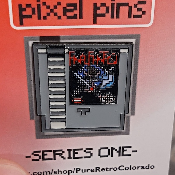 May include: A red card with white text that reads "pixel pins" and a pixelated image of a Nintendo Entertainment System game cartridge with the title "Mega Man 2". The text below the image reads "SERIES ONE" and "com/shop/PureRetroColorado".