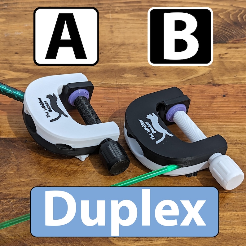 K&ouml;nnte beinhalten: Zwei Klemmen, eine wei&szlig;e und eine schwarze, mit einem Katzenlogo und dem Text "The Whisker Bazaar". Das Wort "Duplex" steht in einem blauen Rechteck. Jede Klemme hat einen Schraubmechanismus und ein gr&uuml;nes Rohr.