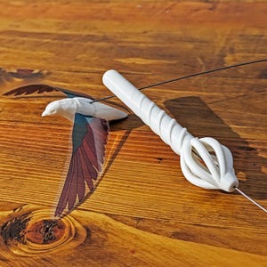 May include: A white plastic bird toy with a clear plastic wing and a red and blue design. The toy is attached to a white plastic string with a white plastic handle.