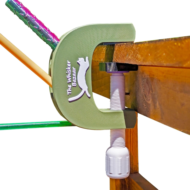 K&ouml;nnte beinhalten: Eine gr&uuml;ne C-Klemme mit dem Text "The Whisker Bazaar" und einem wei&szlig;en Katzenlogo h&auml;lt ein Holzbrett fest. Die Klemme hat eine wei&szlig;e Gewindestange und einen wei&szlig;en Griff. Farbige St&auml;be werden in der Klemme gehalten.