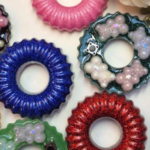 Pode incluir: Close-up de várias peças de resina coloridas com um design circular. As peças são em várias cores, incluindo rosa, azul, vermelho e verde, com detalhes em glitter. Algumas peças têm enfeites em forma de urso.