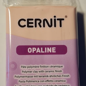 Może przedstawiać: Blok jasnoróżowej gliny polimerowej z nadrukowaną nazwą marki "CERNIT" i słowem "OPALINE" na przodzie. Opakowanie zawiera również tekst "Pâte polymère finition céramique", "Polymer clay with ceramic finish", "Polymermasse mit keramik-ähnliches Finish", "Pasta Polimerica con effetto ceramica", i "Arcilla polimérica con acabado de cerámico".