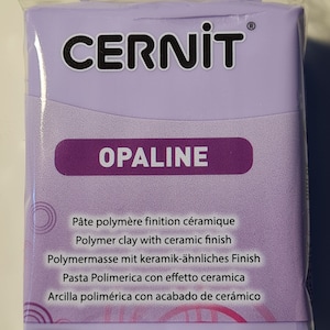 Może przedstawiać: Fioletowe opakowanie gliny polimerowej CERNIT OPALINE z ceramicznym wykończeniem. Opakowanie zawiera tekst w kilku językach opisujący produkt.