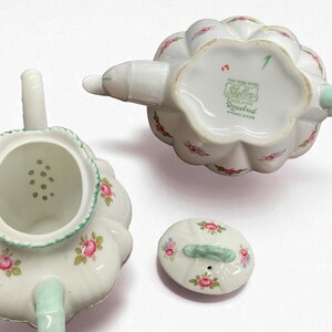 May include: A white porcelain teapot set with a floral rosebud pattern. The set includes the teapot, lid, and a strainer. The teapot has a scalloped edge and a mint green handle and spout. The underside of the teapot has the text "Shelley England Rosebud".