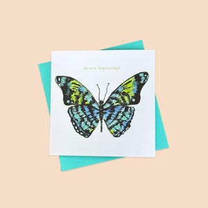 May include: A white card with a blue and green butterfly illustration and the text "to new beginnings". The card is on top of a turquoise envelope.