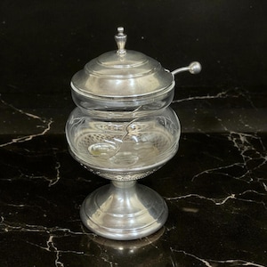 May include: Silver sugar bowl with a glass insert and a silver lid. The bowl has a decorative etched design and a silver base.