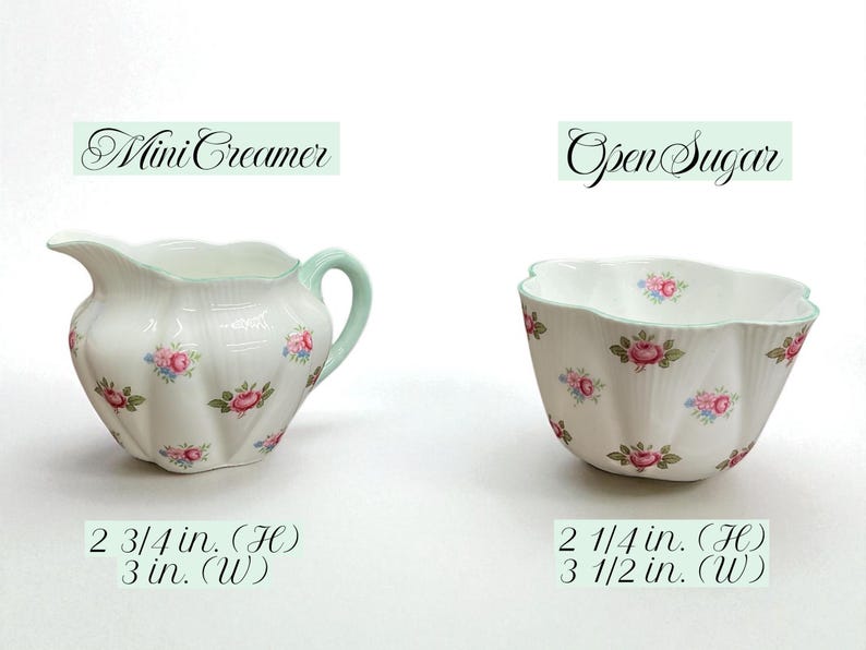 May include: A white porcelain mini creamer and open sugar bowl set. The creamer has a mint green handle and rim, and the sugar bowl has a scalloped edge. Both are decorated with pink and blue rose clusters. The creamer is 2 3/4 inches high and 3 inches wide. The sugar bowl is 2 1/4 inches high and 3 1/2 inches wide.