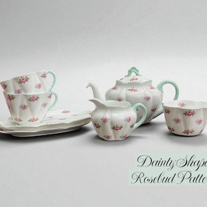 Könnte beinhalten: Weißes Porzellan-Teeservice mit Rosenknospenmuster, einschließlich Tassen, Untertassen, Teekanne, Sahnekännchen und Zuckerdose. Die Griffe und Akzente sind helltürkis. Der Text "Dainty Shape Rosebud Pattern" ist sichtbar.
