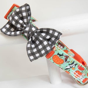 May include: A black and white checkered bow tie attached to a teal and orange dog collar with a pumpkin and apple print.
