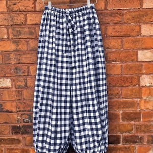 May include: Wide-leg trousers featuring a navy blue and white gingham check pattern. The garment has an elasticated waistband with a matching fabric drawstring tie and gathered, cinched cuffs at the bottom with small ties on each leg.