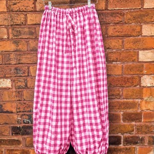 May include: Wide-leg trousers featuring a vibrant pink and white gingham check pattern. The pants have an elasticized waistband with a matching fabric drawstring tie and gathered, cinched cuffs at the bottom with small ties on each leg.