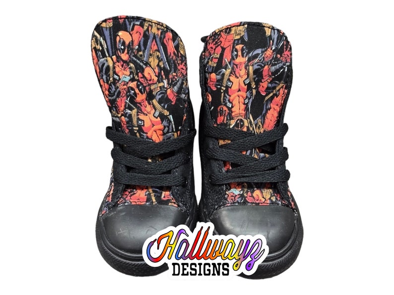 May include: Black high-top sneakers with a red and black Deadpool print. The shoes have black laces and a black rubber sole.