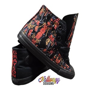 May include: Black high-top sneakers with a red and black Deadpool print. The sneakers have black laces and a white sole. The text "GRAYSON" is printed on the side of the sneakers.