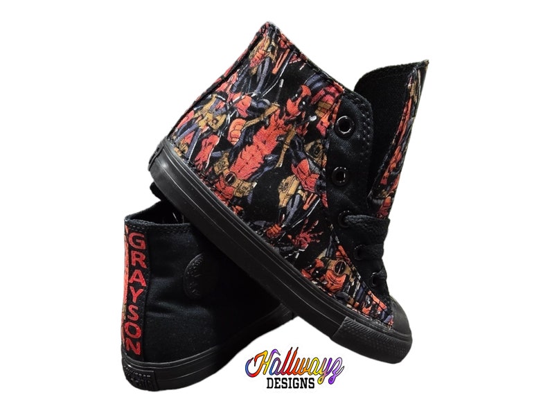 May include: Black high-top sneakers with a red and black Deadpool print. The sneakers have black laces and a white sole. The text "GRAYSON" is printed on the side of the sneakers.
