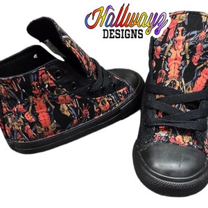 May include: Black high-top canvas shoes with a print of Deadpool characters. The shoes have black laces and a black rubber sole.