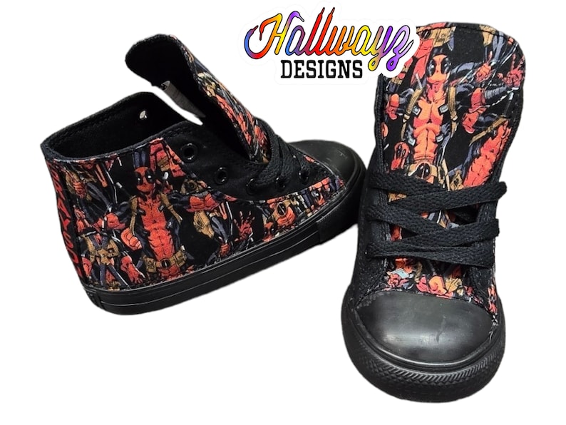 May include: Black high-top canvas shoes with a print of Deadpool characters. The shoes have black laces and a black rubber sole.